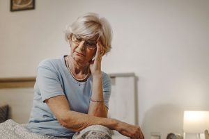 Senior woman having a headache and holding her head in pain while sitting on the bed at night.