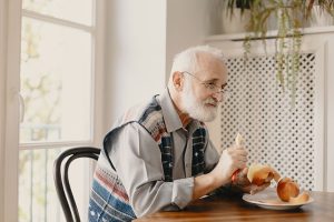 Lonely elderly man eating an apple by the table in empty home